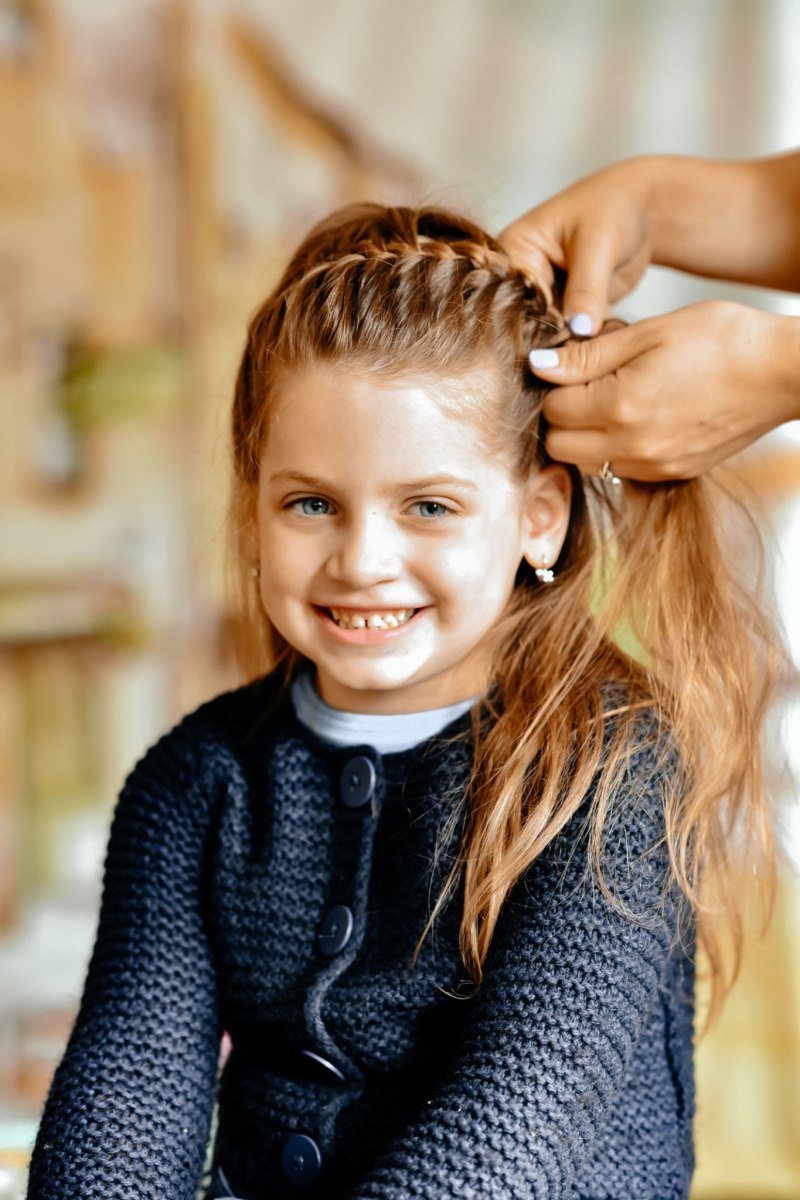 Mother styling a braided spikelet and flipped sections on her daughter's hair