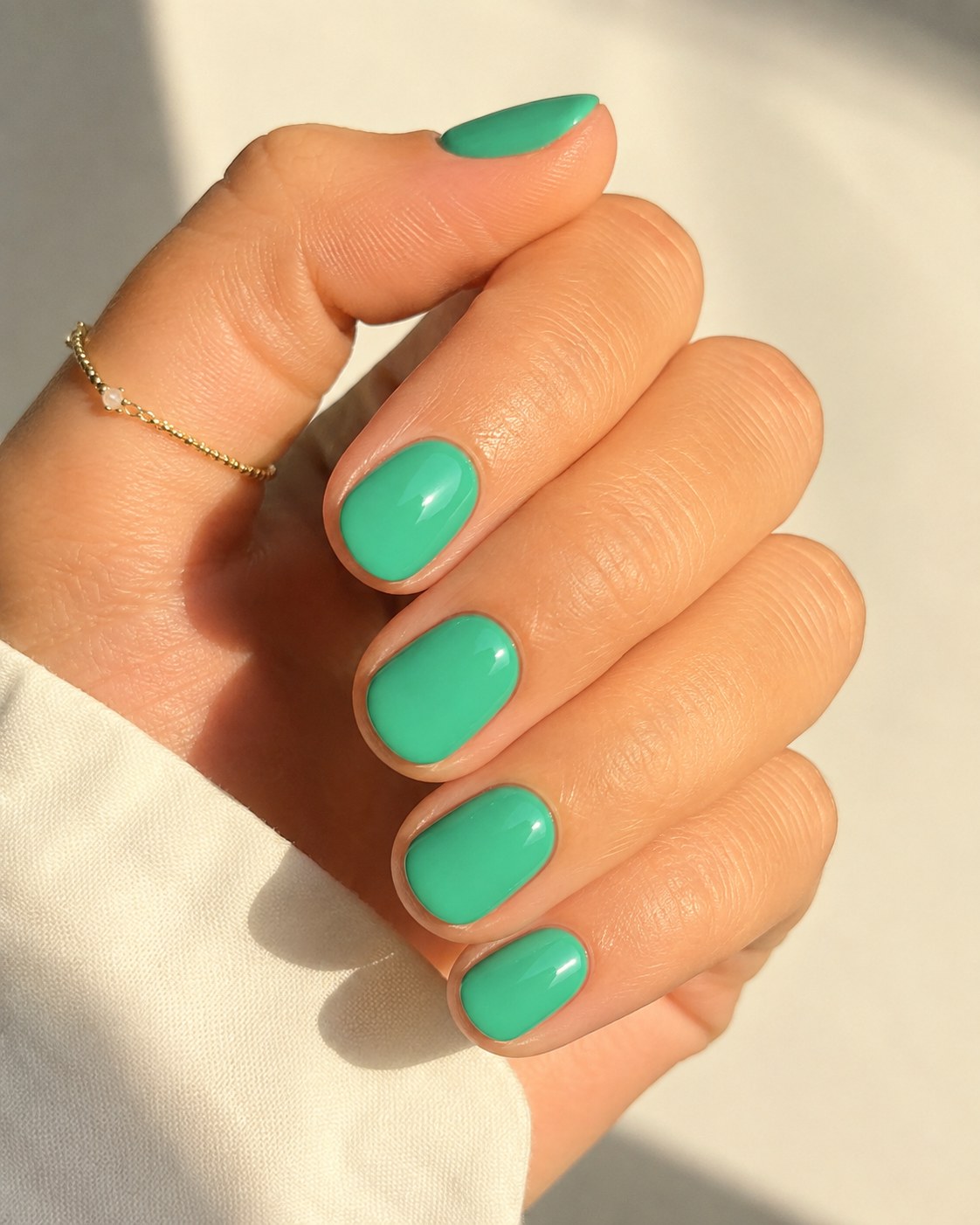 Bright jade green nail polish on short round nails with a delicate gold bracelet