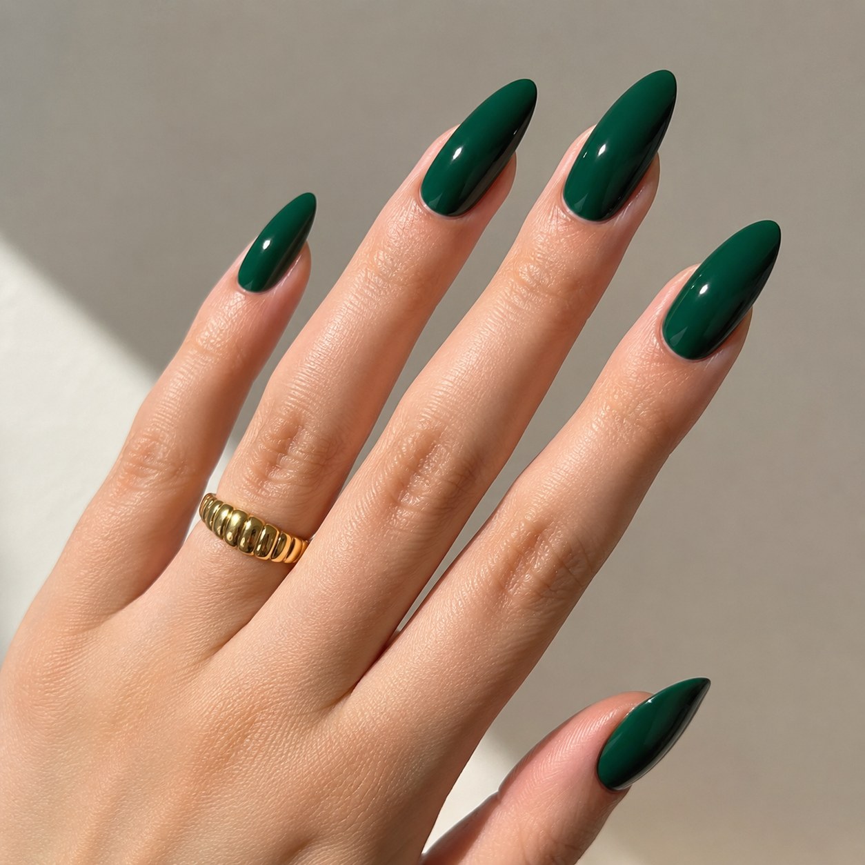 Glossy emerald green nail polish on almond-shaped nails accented with a gold ring