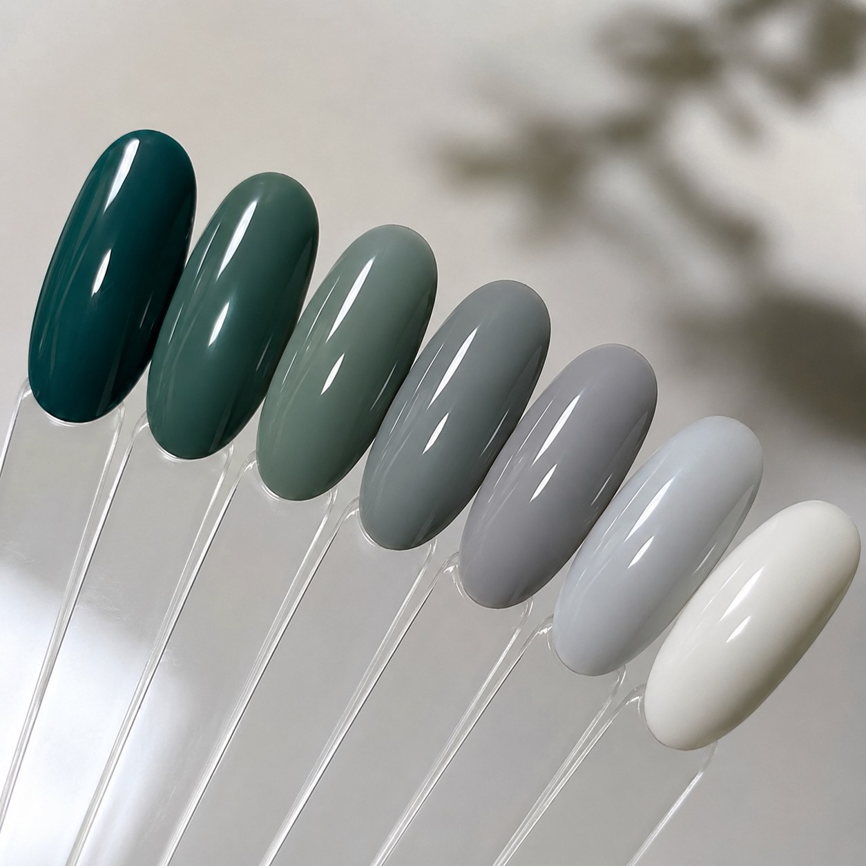 Swatch fan of green nail shades fading from deep teal through sage to soft grey