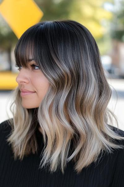 A woman with wavy shoulder-length black hair, styled with blonde highlights and full, fringe bangs.