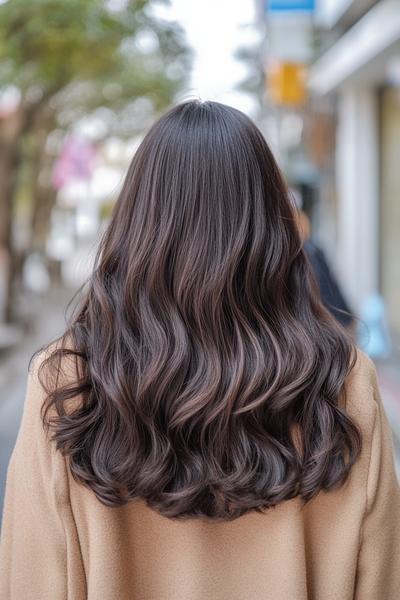 A person with flowing, dark brown hair styled in loose waves, seen from behind.