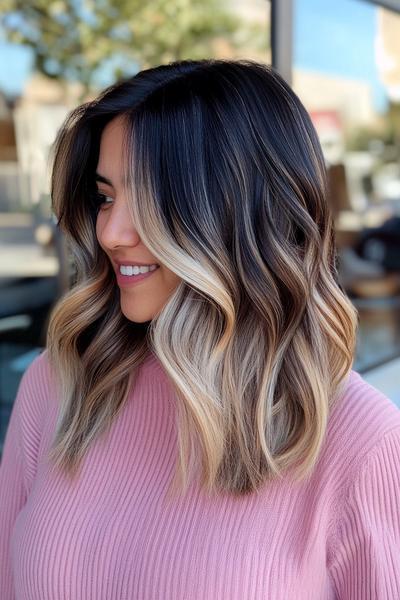 A woman with shoulder-length black hair featuring blonde highlights styled in loose waves.