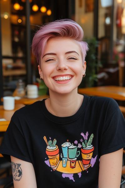 A woman with a pink undercut pixie haircut smiles brightly while wearing a black graphic T-shirt.