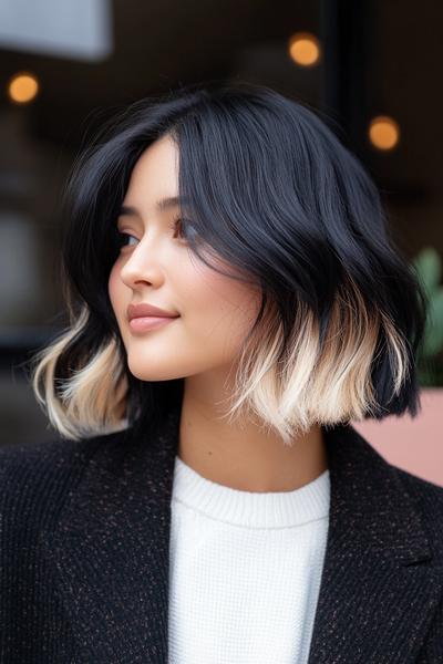 A woman with a chic bob hairstyle featuring rich black hair and striking blonde highlights towards the ends.