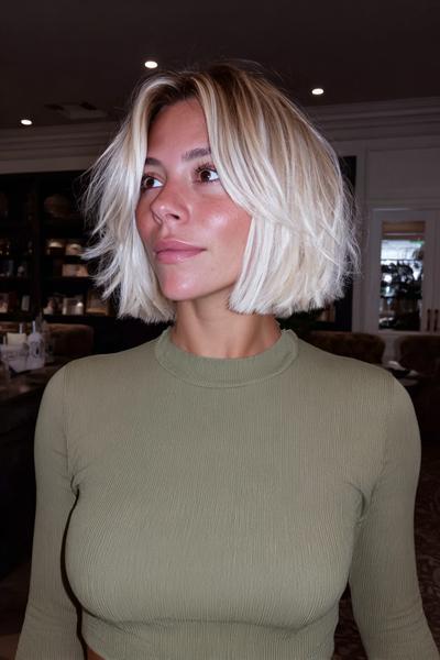 A woman with a chin-length, blunt bob haircut featuring textured, tousled layers and a centre parting, but without a fringe.