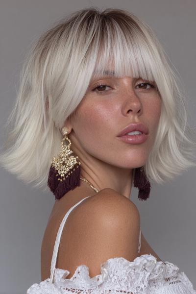 A woman with a chin-length platinum blonde bob hairstyle featuring straight, full fringe across the forehead.