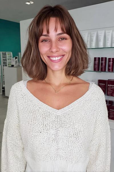 A woman with a chin-length wavy bob haircut featuring soft, wispy fringe across her forehead.