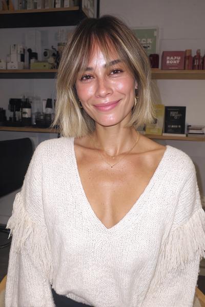 A woman with a textured bob haircut featuring soft, wispy fringe that frames her face, with natural-looking blonde highlights.