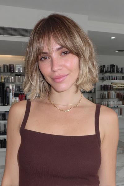 A woman with a textured, chin-length bob haircut featuring soft, wispy fringe across the forehead.