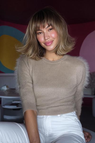 A woman with a softly textured bob haircut featuring voluminous, bouncy layers and a wispy fringe, styled in a natural, tousled look.