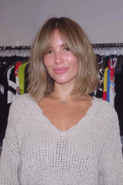 A woman with a textured, shoulder-length bob haircut and soft, wispy fringe stands in front of a clothes rail.