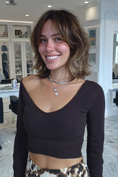A woman with a tousled chin-length bob hairstyle featuring soft, wispy fringe across her forehead.