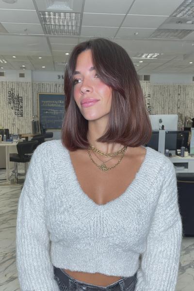 A woman with a sleek, chin-length bob haircut featuring subtle curtain bangs, styled straight and parted down the middle.