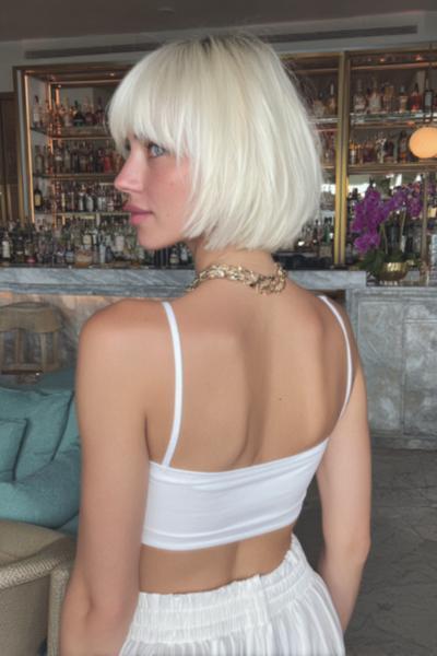 A woman with platinum blonde hair wears a classic bob haircut with straight, full fringe, styled to fall just below the jawline.