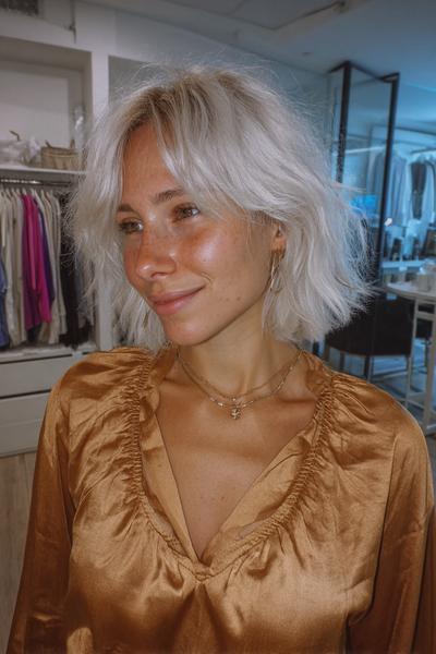 A woman with platinum blonde, tousled bob hair featuring soft, wispy fringe.