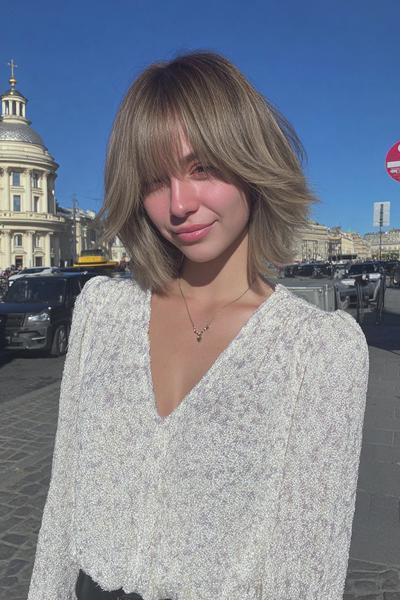 A young woman with a textured bob haircut featuring choppy layers and a wispy fringe, styled in a natural, slightly tousled look.