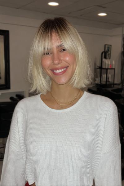 A woman with a chin-length blonde bob haircut featuring full, wispy fringe.
