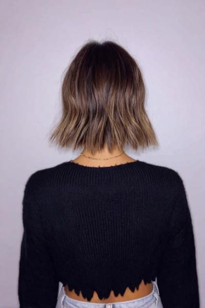 A woman with a blunt, chin-length bob haircut with subtle waves and light brown highlights, viewed from the back.