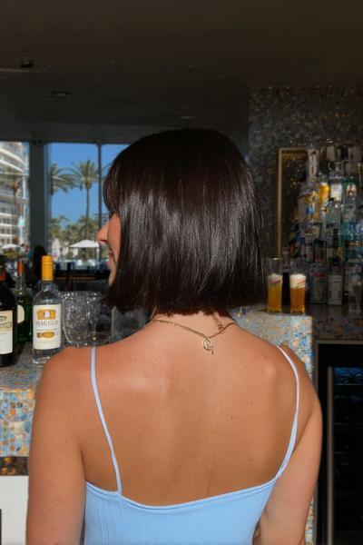 A woman with straight, dark brown hair styled in a classic bob with a full fringe, seen from behind.