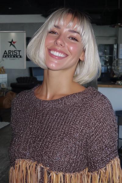 A smiling woman with a sleek, chin-length bob haircut and straight, eyebrow-grazing fringe.