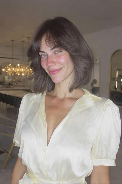 A woman with a chin-length bob haircut featuring soft, wispy fringe framing her face.