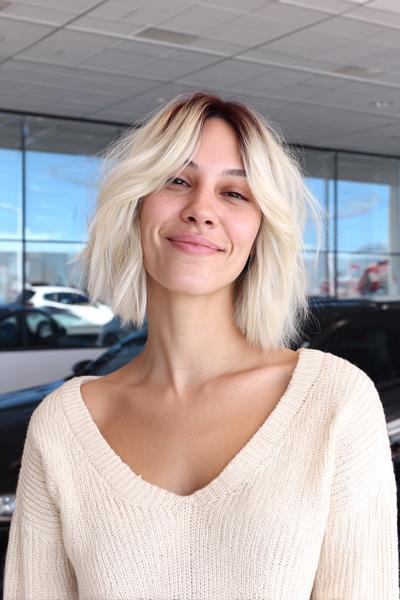 A woman with a chin-length, tousled bob haircut featuring soft, face-framing fringe and platinum blonde highlights.