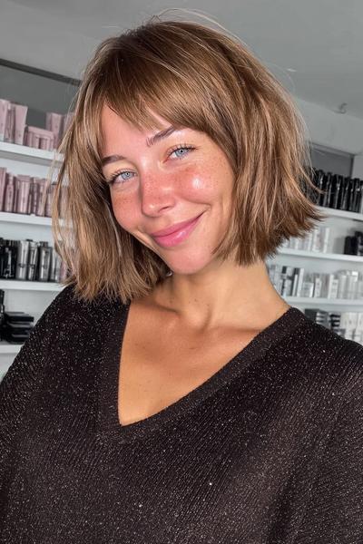 A woman with a textured bob haircut featuring soft, tousled waves and wispy fringe.
