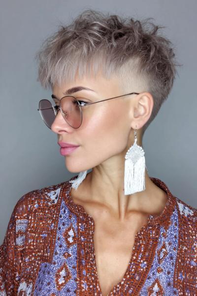 A woman with a textured, platinum blonde undercut pixie hairstyle, featuring short sides and longer, tousled hair on top.