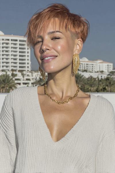 A woman with a textured, copper-coloured undercut pixie hairstyle, featuring longer tousled layers on top and closely cropped sides.