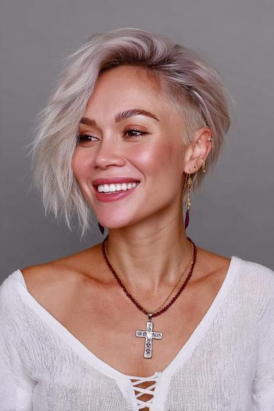 A woman with platinum blonde hair styled in an undercut pixie cut, featuring long, textured layers swept to one side and closely cropped sides.