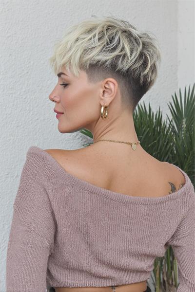 A woman with a short, textured platinum blonde pixie cut featuring a dark undercut at the back and sides.