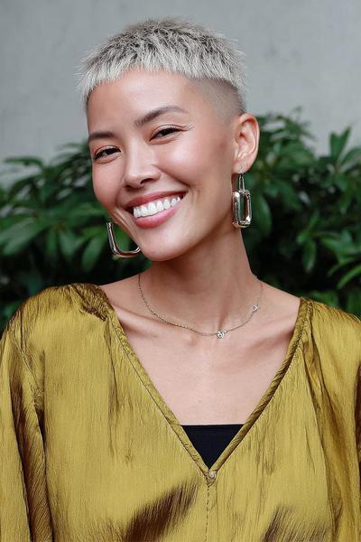 A woman with platinum blonde hair styled in a very short undercut pixie, featuring closely cropped sides and back with slightly longer textured hair on top.