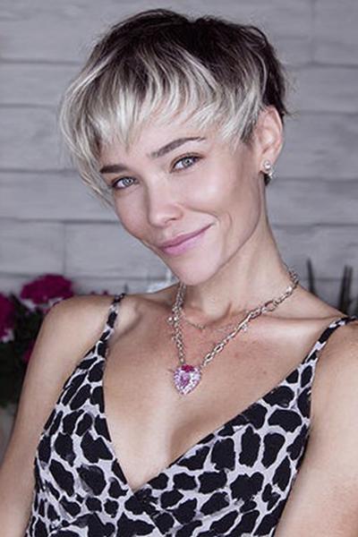 A woman with an undercut pixie hairstyle featuring dark sides and back, with longer, textured top layers in light blonde and natural roots, styled forward with choppy fringe.