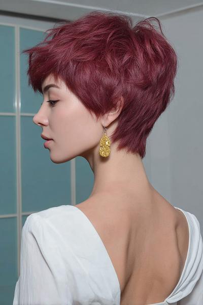 A woman with short, textured burgundy hair styled in an undercut pixie cut, with the sides closely cropped and the top left voluminous and tousled.