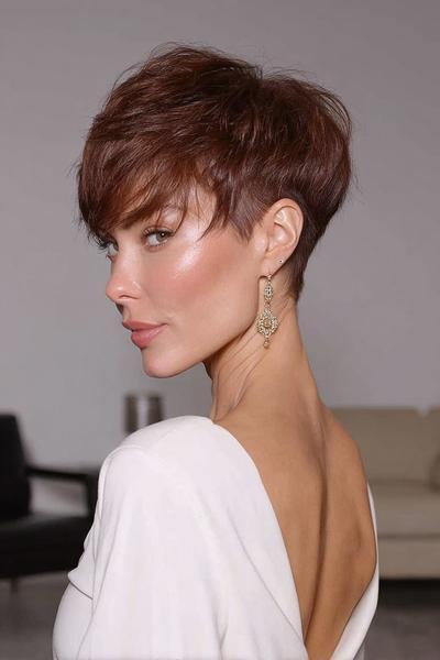 A woman with short, textured brown hair styled in an undercut pixie cut, with longer layers on top and closely cropped sides, is shown in a side profile view.