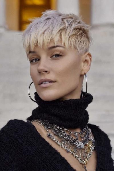 A woman with a platinum blonde undercut pixie hairstyle featuring textured layers on top and short, tapered sides.