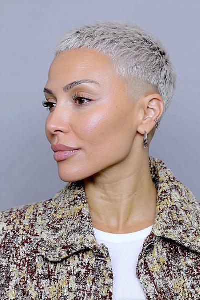 A woman with platinum blonde hair wears an undercut pixie hairstyle, featuring closely cropped sides and slightly longer textured hair on top.