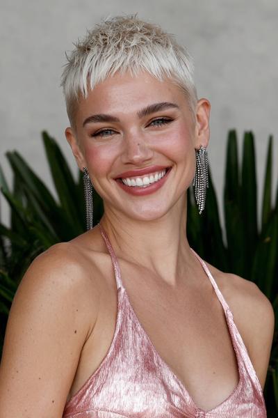 A woman with platinum blonde hair is wearing a textured undercut pixie hairstyle, featuring very short sides and slightly longer, choppy layers on top.