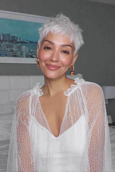 A woman with short, textured, platinum blonde hair styled in an undercut pixie cut, featuring closely-cropped sides and longer layers on top.
