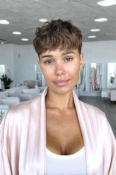 A woman with a short undercut pixie hairstyle featuring closely cropped sides and back with longer, textured hair on top and a soft fringe at the front.