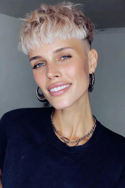 A woman with a platinum blonde undercut pixie hairstyle, featuring short, textured layers on top and closely shaved sides.