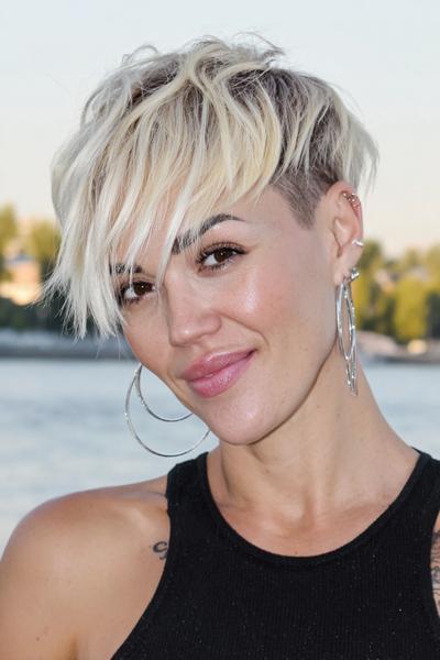 A woman with a short, textured undercut pixie hairstyle featuring platinum blonde layers on top and darker shaved sides.