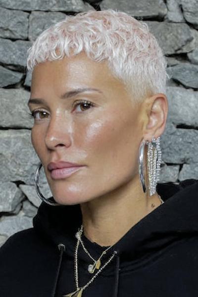 A woman with a platinum blonde undercut pixie hairstyle featuring short, textured curls on top and closely shaved sides.