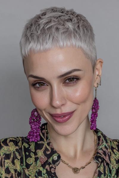 A woman with a platinum blonde undercut pixie hairstyle, featuring closely cropped sides and back with slightly longer textured hair on top.