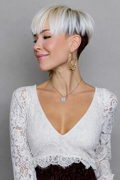 A woman with a platinum blonde undercut pixie hairstyle featuring longer, textured layers on top and closely cropped dark hair underneath.