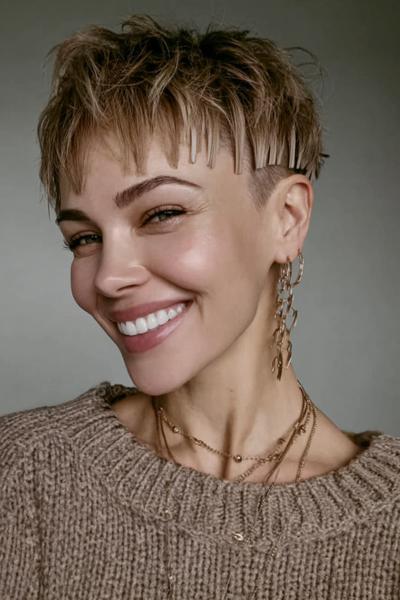 A woman with a textured, tousled pixie cut featuring a shaved undercut on the sides and metallic hair clips accenting the fringe.