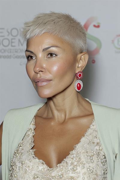 A woman with a platinum blonde, very short undercut pixie hairstyle featuring closely cropped sides and slightly longer textured layers on top.