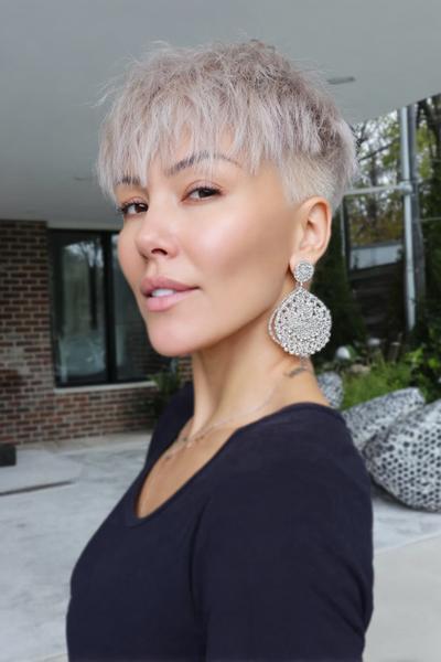 A woman with a short, platinum blonde undercut pixie hairstyle featuring textured layers on top and closely cropped sides is posing outdoors.