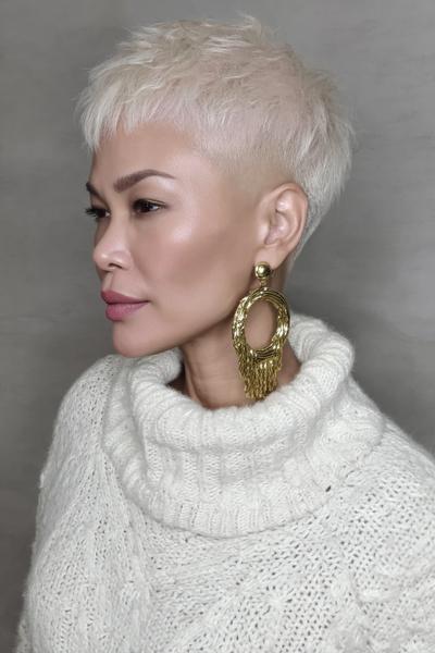 A woman with platinum blonde hair wears a textured undercut pixie hairstyle, featuring closely cropped sides and a longer, tousled top.